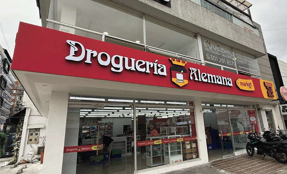 Gran letrero corpóreo iluminado tipo cajón en la fachada de la Droguería Alemana Market, instalado por Bresspop. Presenta letras blancas en relieve sobre un fondo rojo vibrante, con el logo y textos adicionales en acrílico y metal.